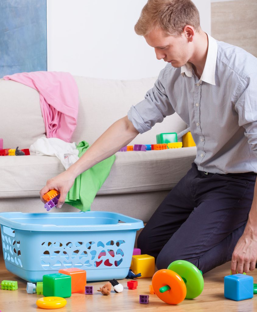 a man picking up toys and putting them into a blue basket