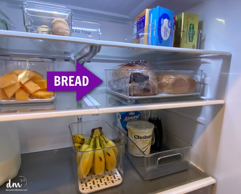 A refrigerator with clear storage bins holding various food items, including a designated section for bread highlighted by a bold purple arrow labeled "BREAD"