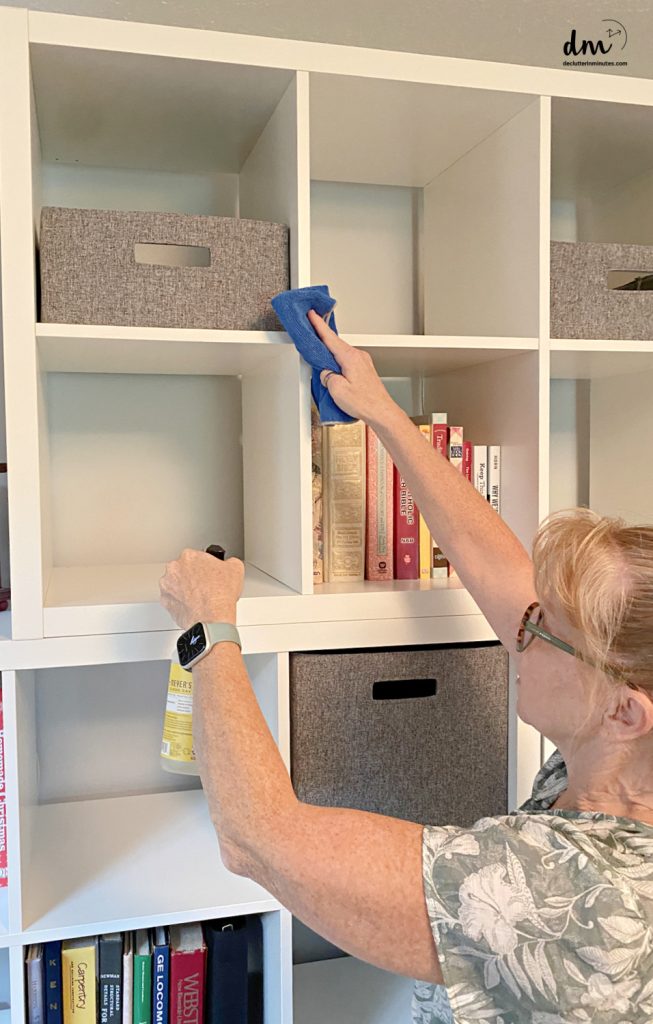 a woman cleaning the high shelves in a home office