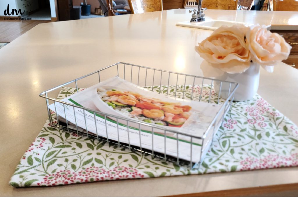 a counter in a kitchen with nothing on it but a flower and a basket of papers