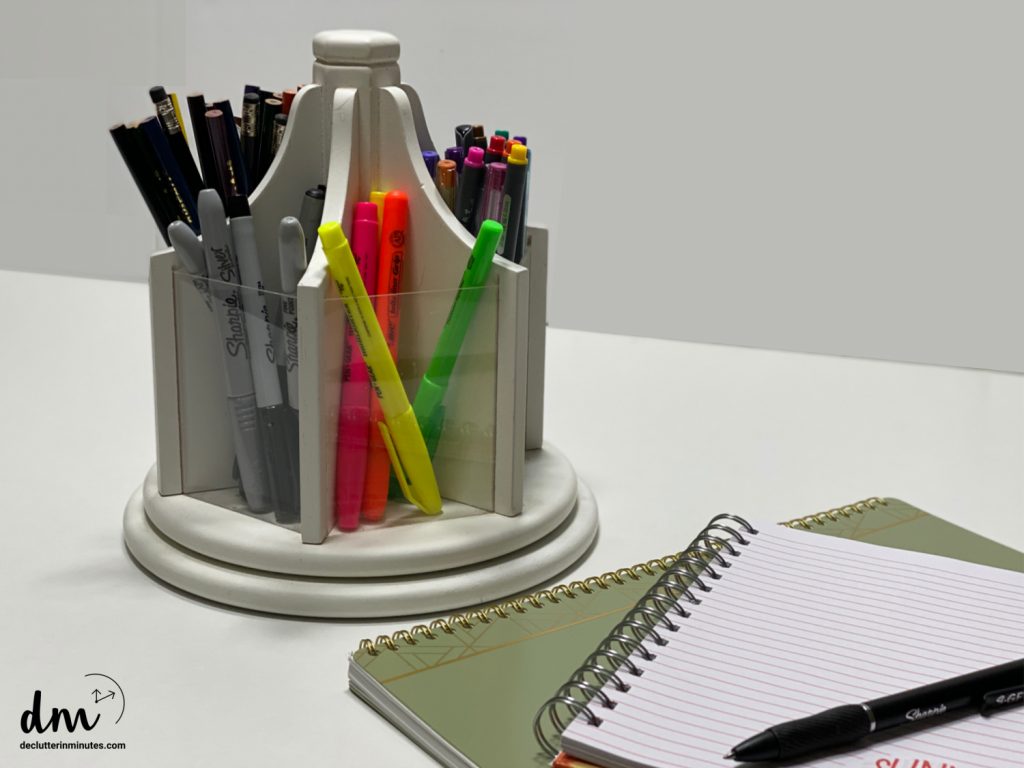 a container holding pens and markers next to a stack of notepads
