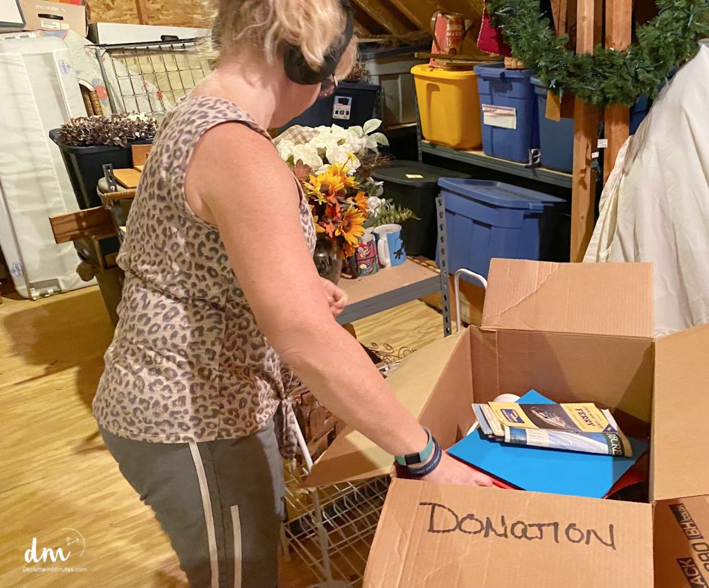 woman putting items into a box labeled donation in a cluttered attic 