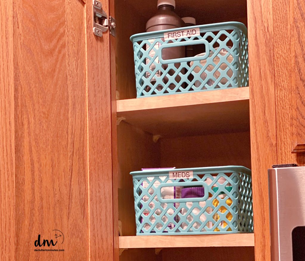 a cabinet in a kitchen with 2 blue baskets labeled meds, first aid