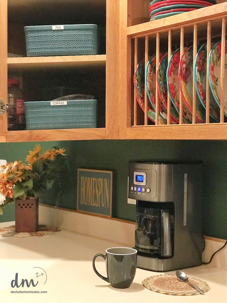 a coffee maker on a counter near baskets and a cup and spoon