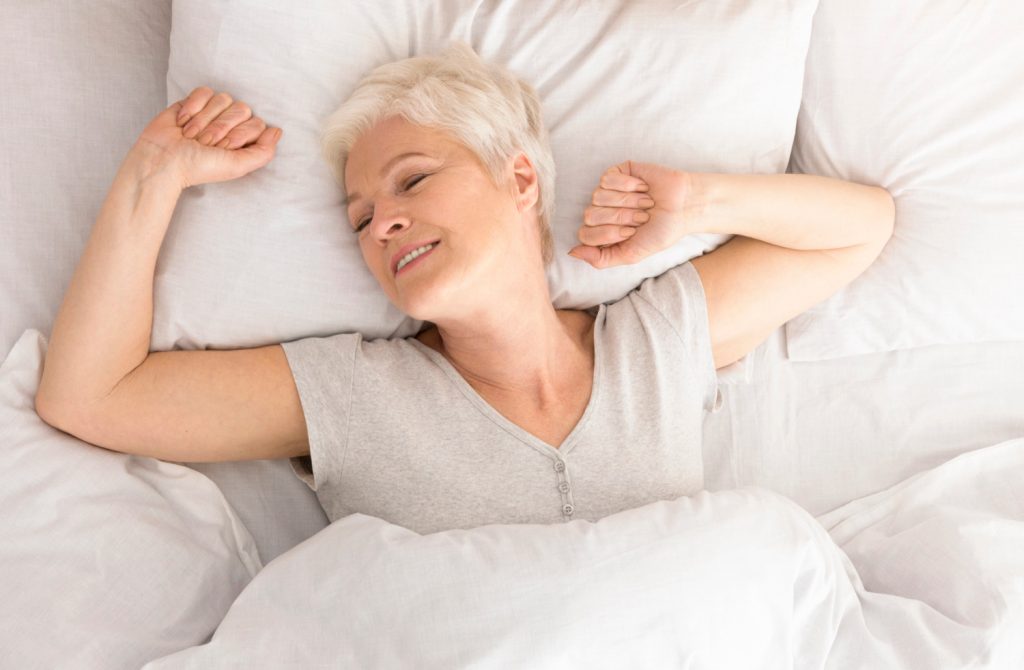 a midlife woman smiling and sleeping in a bed with white bedding