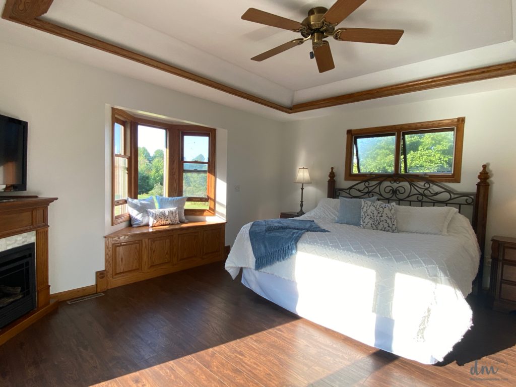 a white bed with a blue blanket in a large bedroom with dark wood floors 