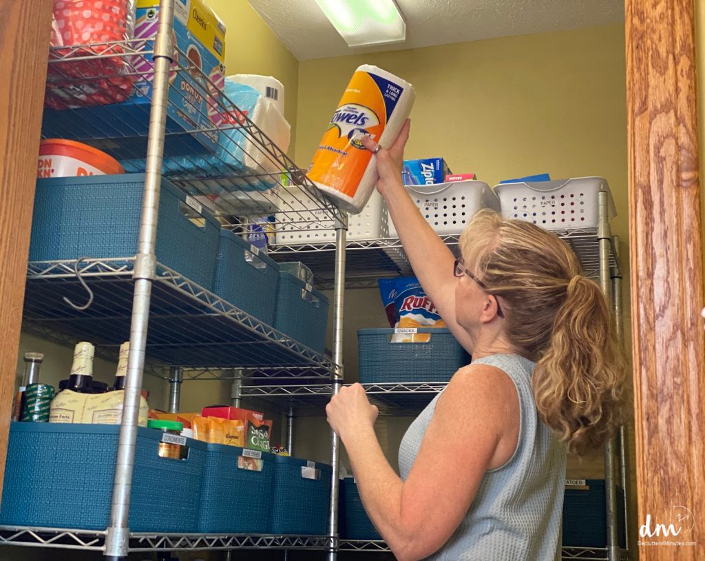 woman returning paper towels to a pantry in a kitchen