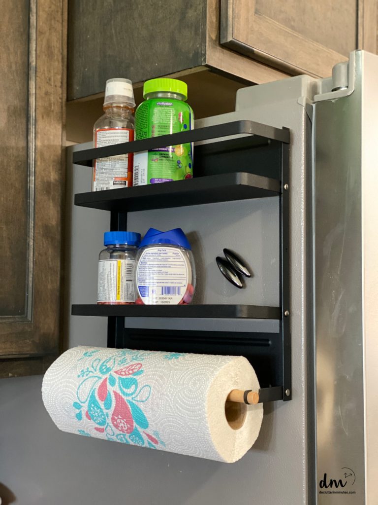 a magnetic shelf on the side of a fridge holding medicines and papertowels