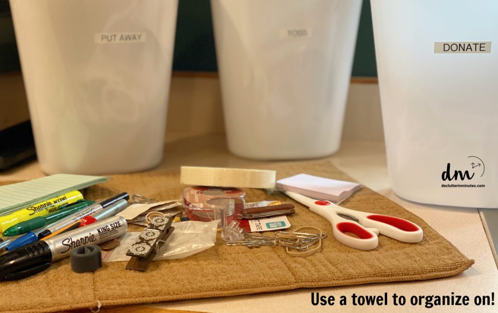 a towel of misc items sitting in front of 3 white trash cans for sorting