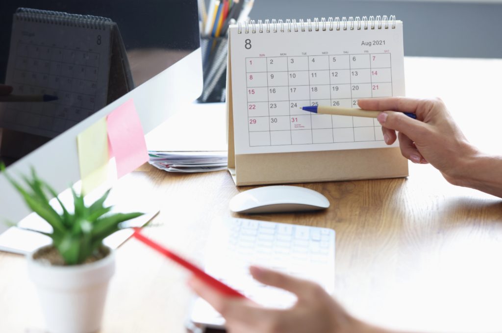 hands pointing a pen to a desk calendar in a home office