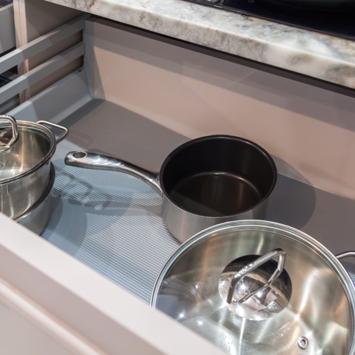 Opened drawer with pots and pans inside in beige kitchen with marble countertop