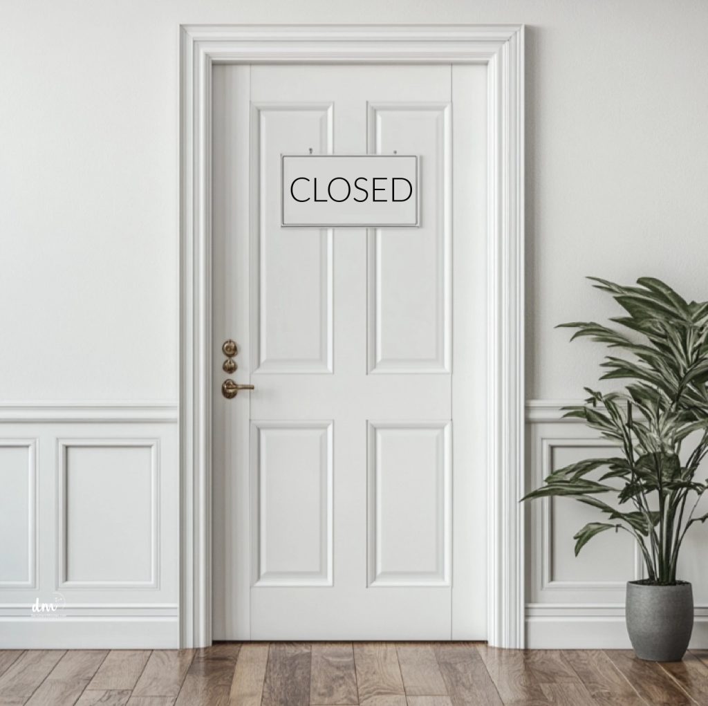 A white door with a "CLOSED" sign, surrounded by elegant paneling and a leafy green plant nearby

