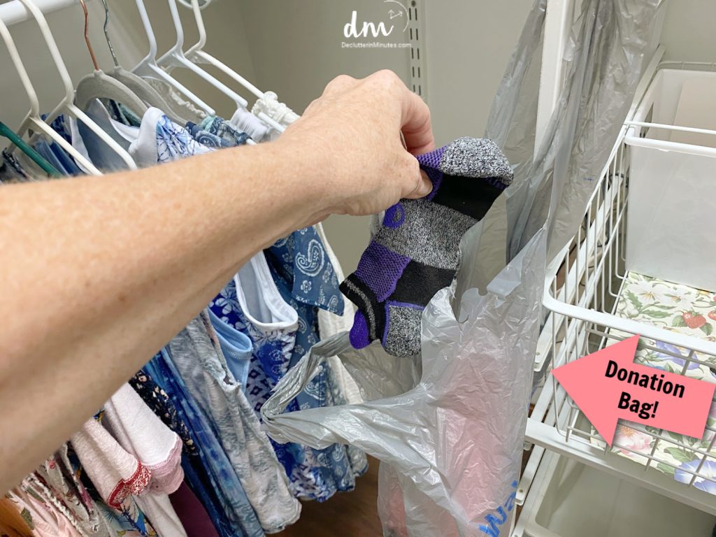 a hand putting socks into a plastic shopping bag in a closet 