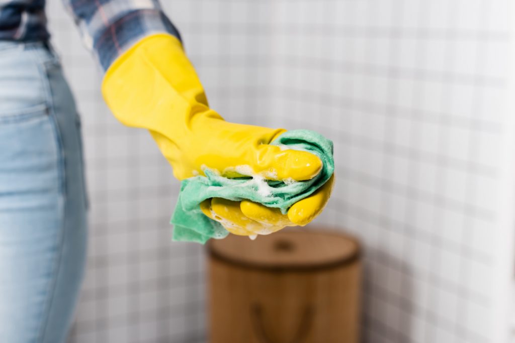 a hand with a yellow glove with a soapy rag for cleaning a bathroom