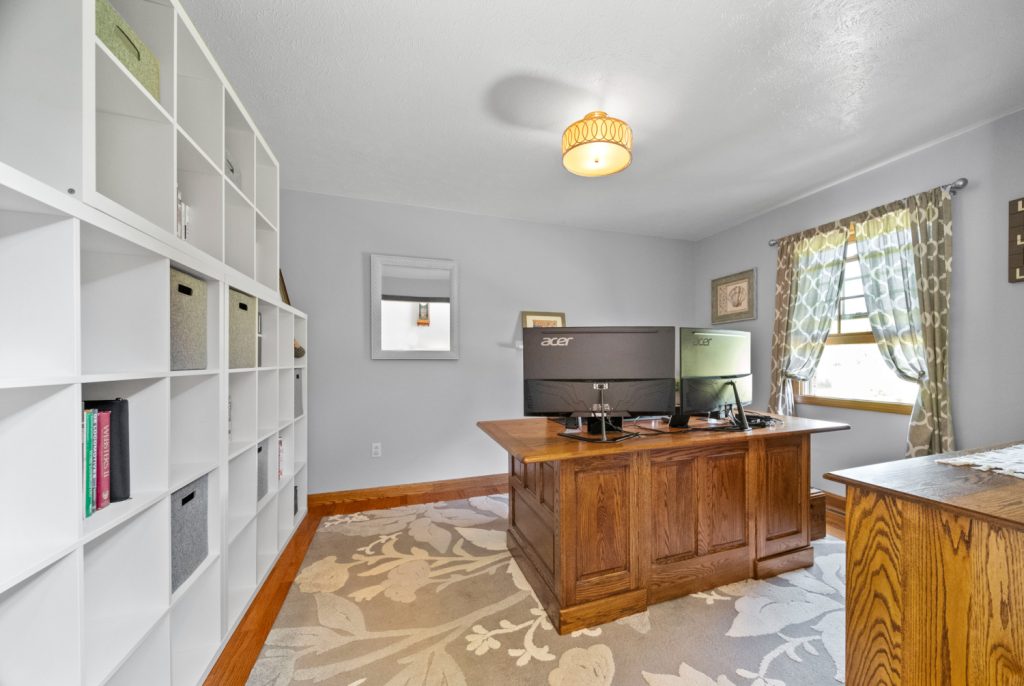 A home office with a wooden desk, dual monitors, and a white shelving unit with storage bins
