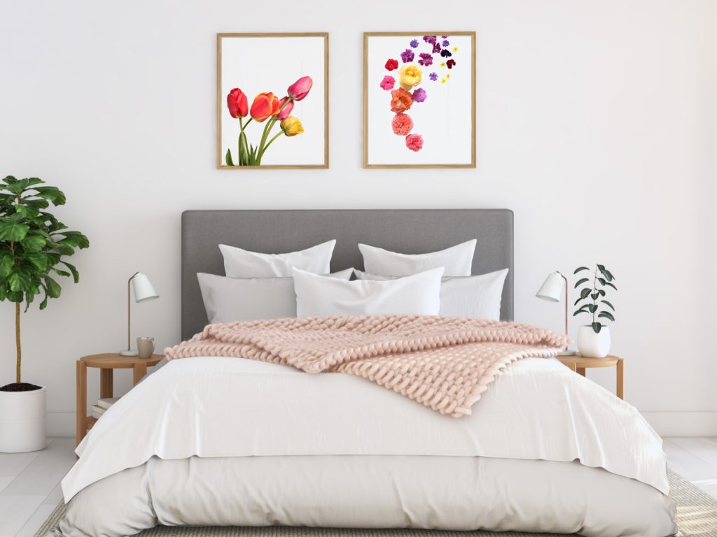 a made bed with lots of pillows with flower pictures on the wall above