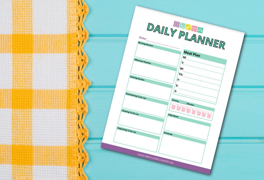 A colorful daily planner worksheet placed on a light blue wooden surface, next to a yellow and white checkered fabric with a crocheted edge