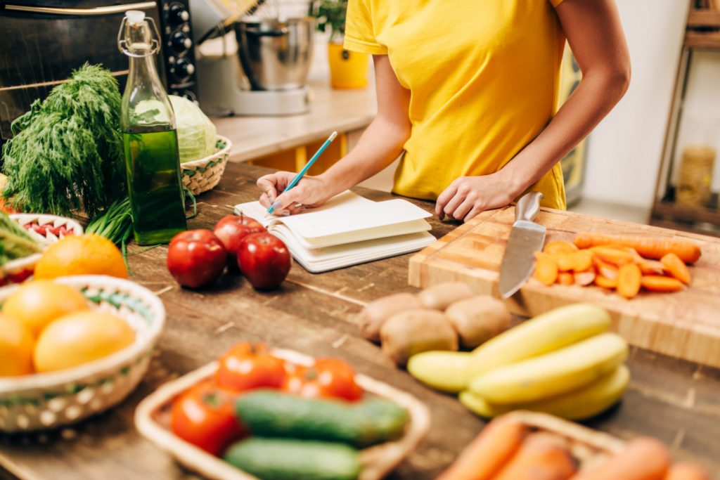 a woman cooking in a kitchen while writing a recipe in a book