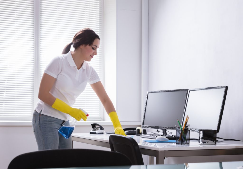 a woman in a white shirt wiping down a desk in a home office