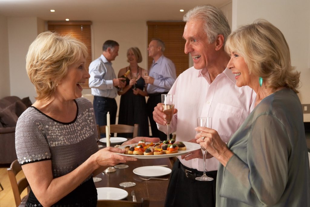 a woman presenting a platter of snacks to a couple of dinner guests