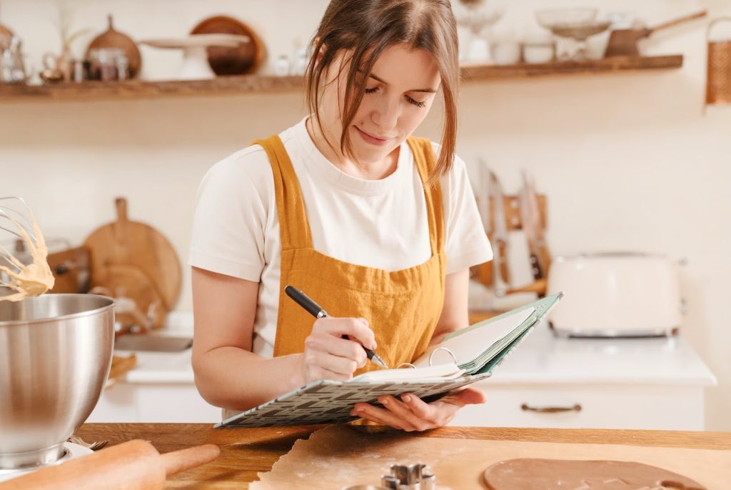 a young woman making notes in a recipe book while baking cookies