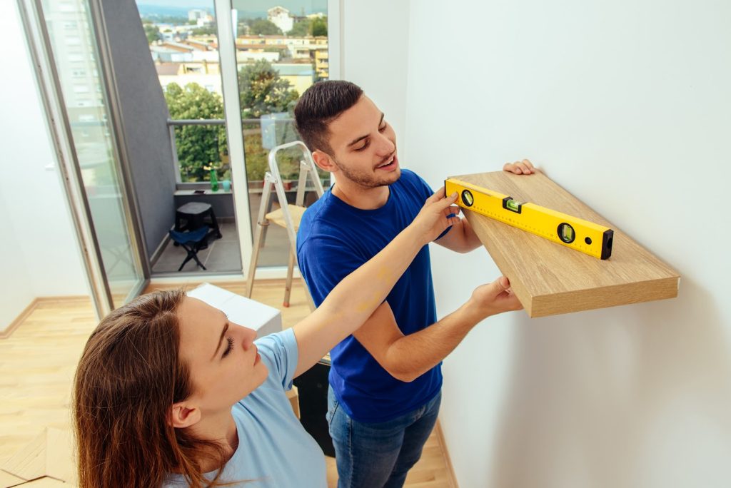 Man and woman putting shelf on the wall at home