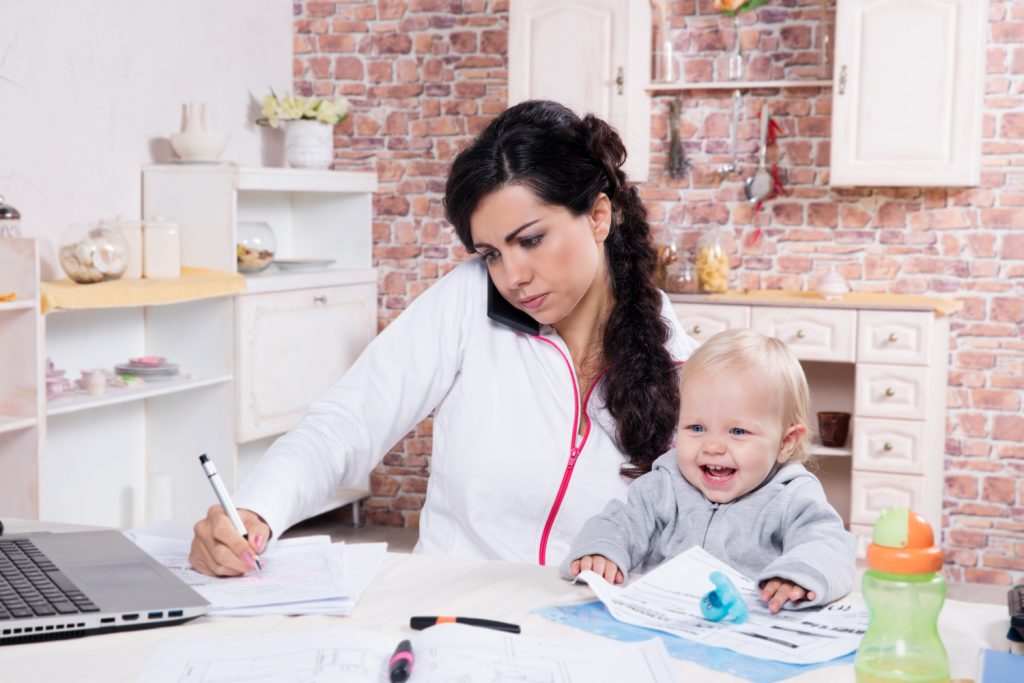 Mother with baby in the kitchen working with documents and speaks by phone