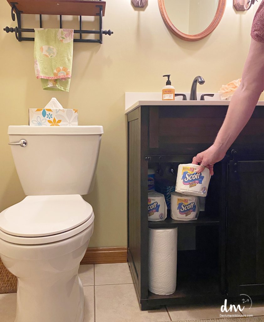 A woman reaching for toilet paper to restock and reset a bathroom