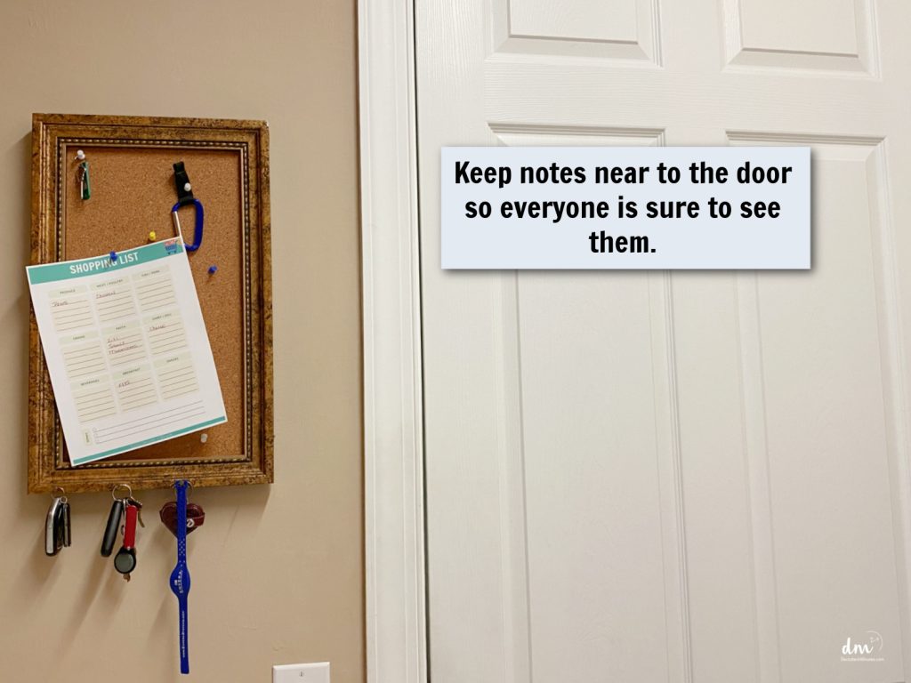 Bulletin board near a door displaying a shopping list, keys, and a reminder to keep notes visible for everyone