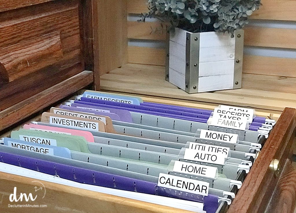 An organized filing system with labeled folders for finances, home, and personal documents, stored in a wooden filing cabinet