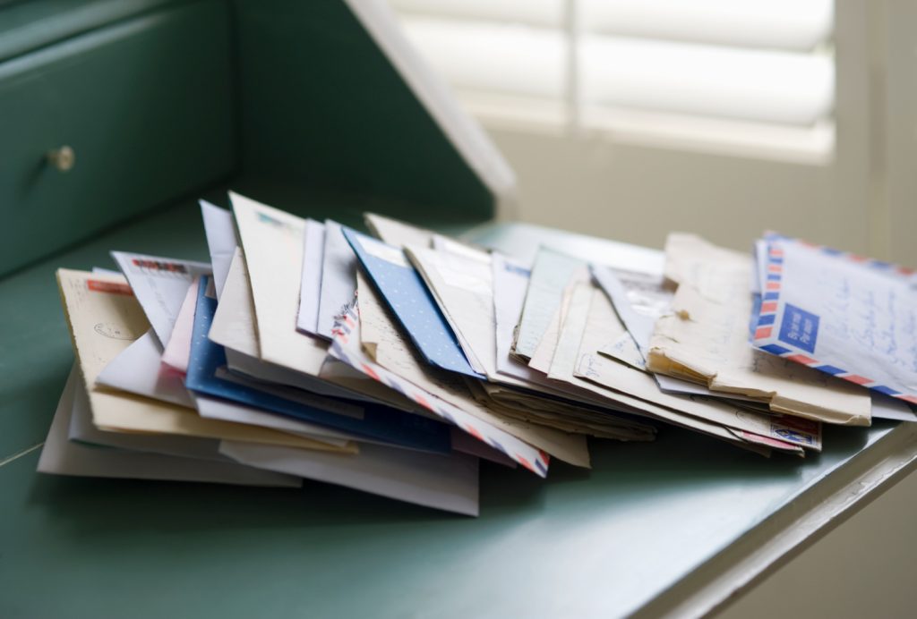 A messy stack of unopened and old letters piled on a green desk