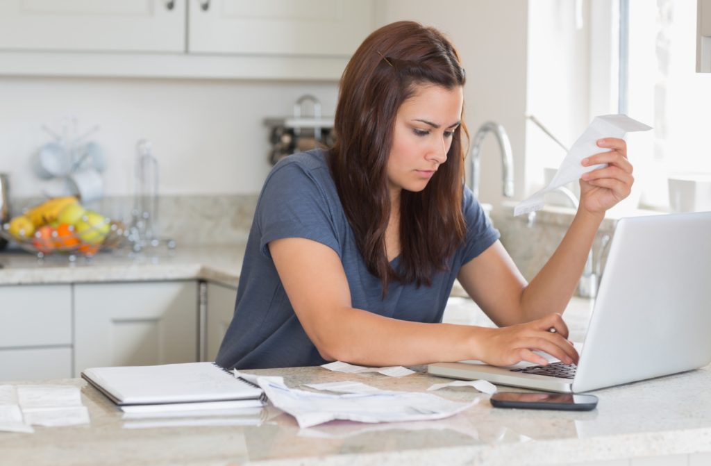 A focused woman sitting at her kitchen counter, reviewing receipts and working on her laptop