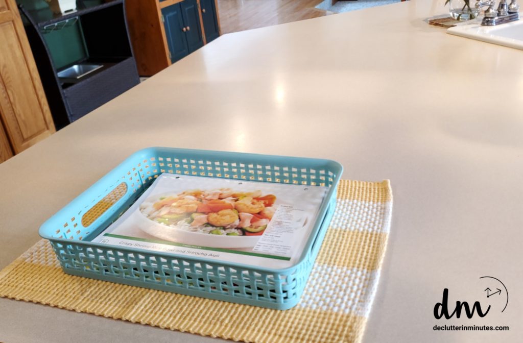 a blue plastic basket on a clutter free kitchen counter full of papers 