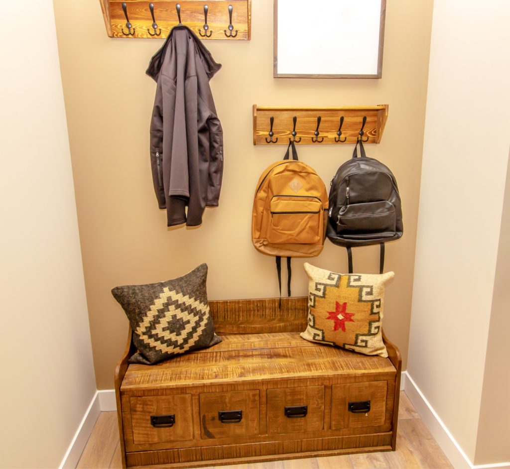 Entryway with a wooden bench, storage drawers, decorative pillows, and hooks holding jackets and backpacks
