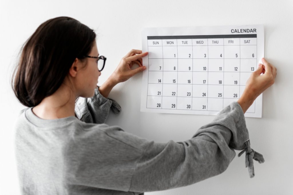 a woman putting a white calendar up on a wall. 