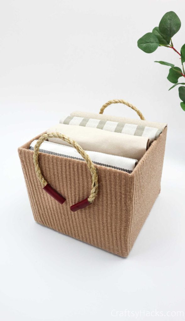 a box turned into a basket using an old sweater and rope as handles.  Basket has bed sheets neatly folded