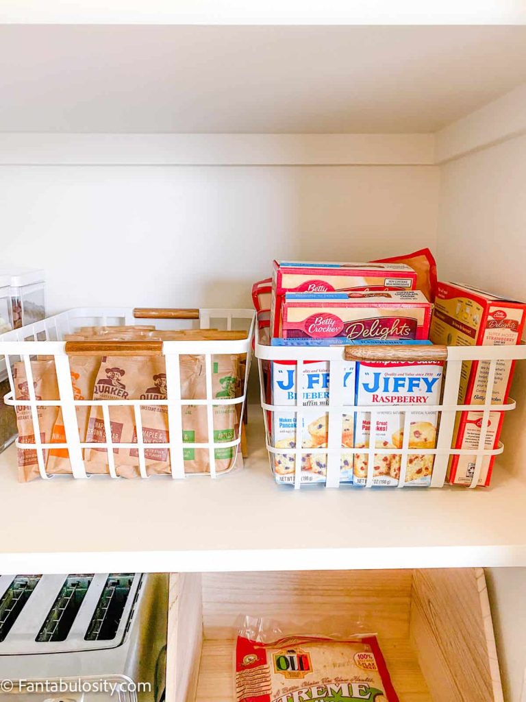 Two white storage baskets holding instant oatmeal packets and baking mixes