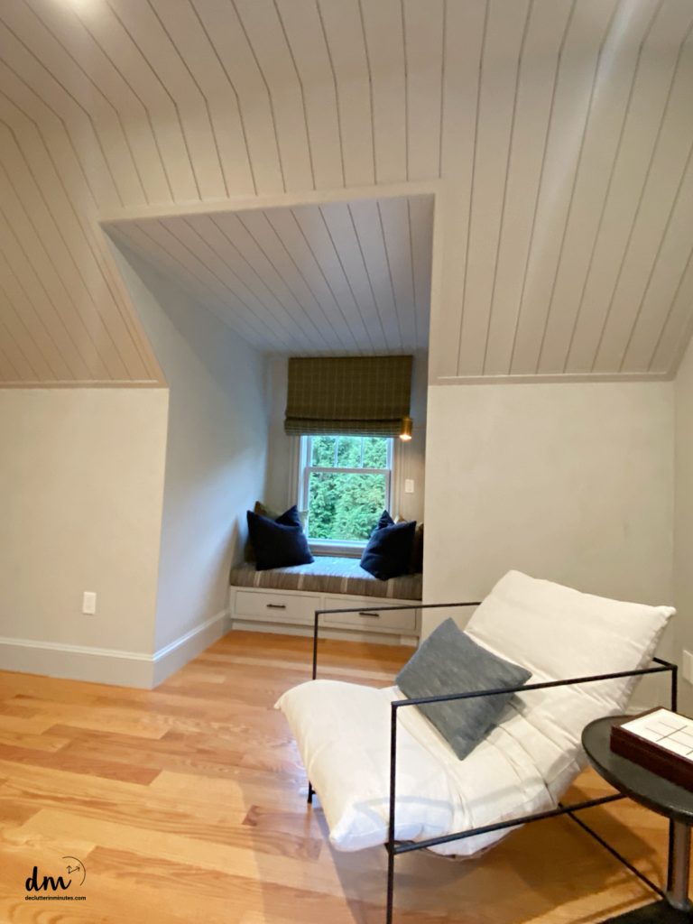 a cozy room in a neat and organized home with a window seat and a white chair