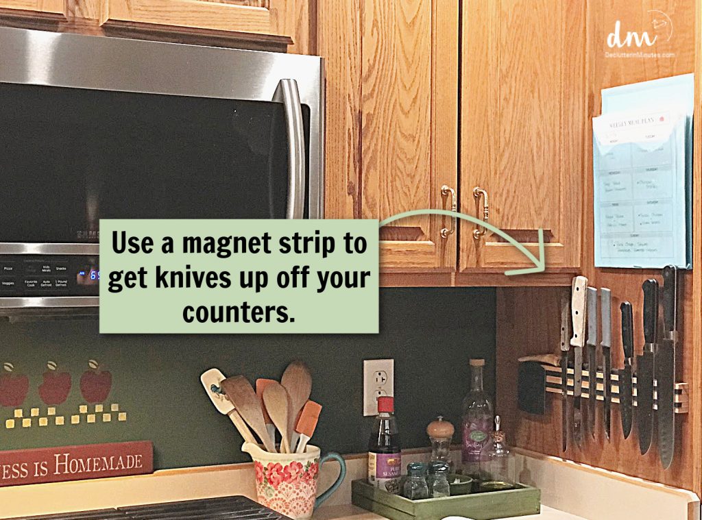 A kitchen corner with a magnetic knife strip mounted on the wall, alongside wooden cabinets, a microwave, and a weekly meal plan