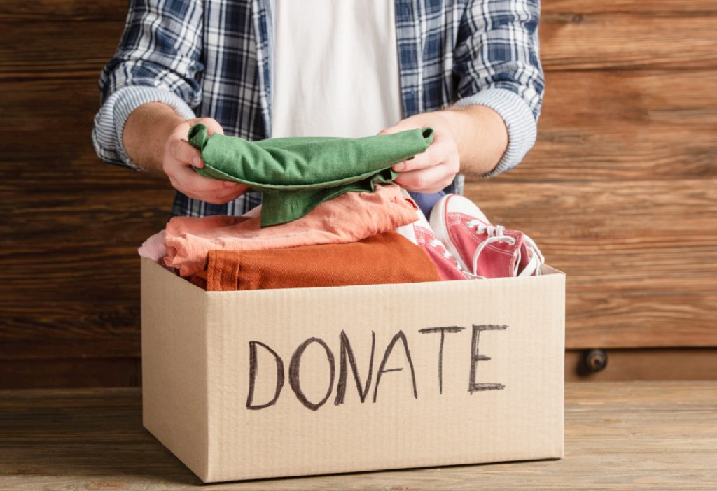hands holding a green shirt over a donation box 
