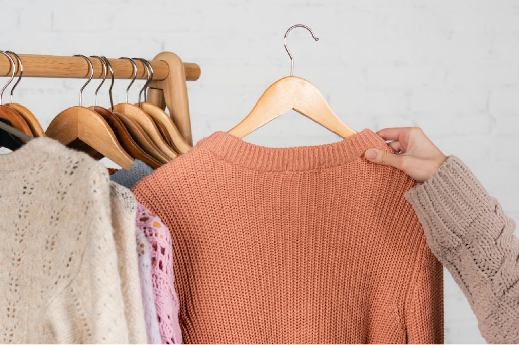 a hand holding a peach sweater on a wooden hanger