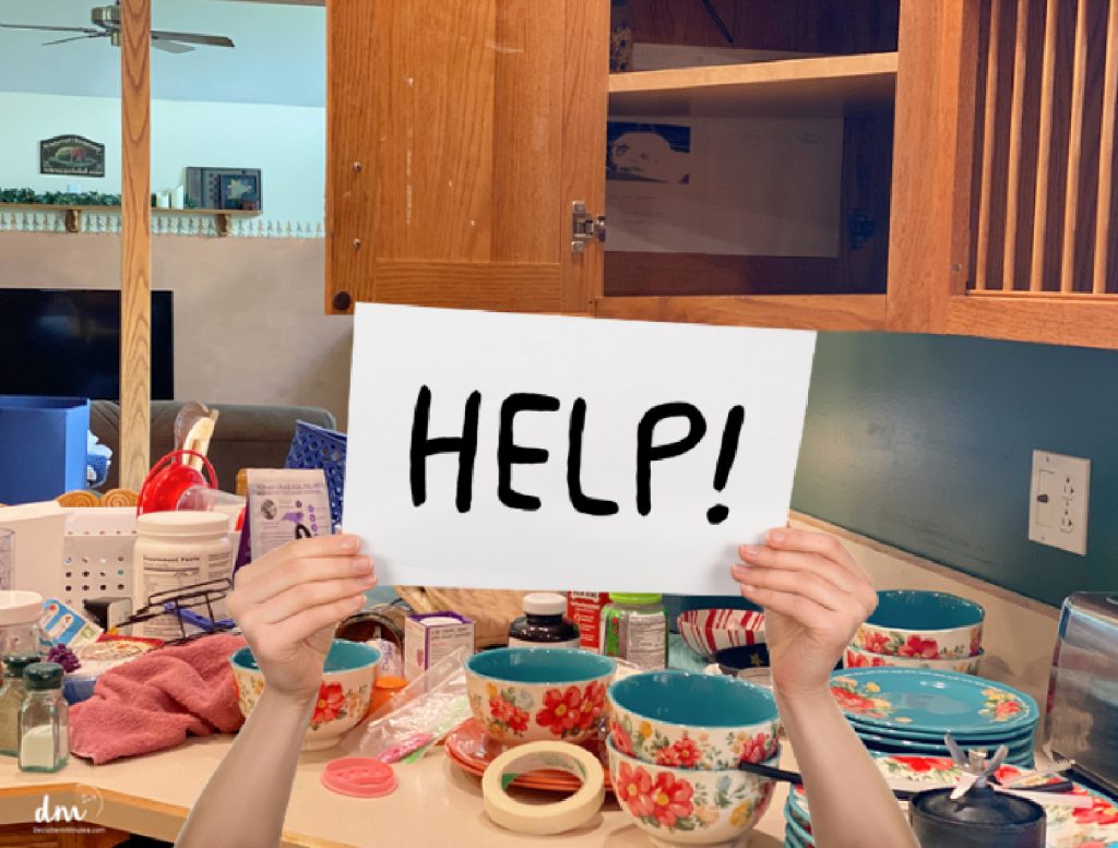 hands holding a HELP sign in front of a messy counter