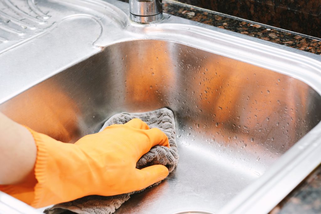 one hand in an orange glove cleaning a kitchen sink