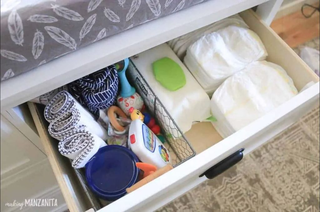 Image that shows a wire basket inside a drawer with baby rattles, creams, and wash cloths.