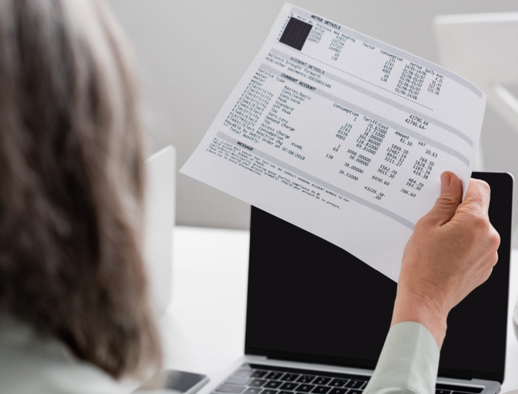 woman holding utility bill in front of laptop
