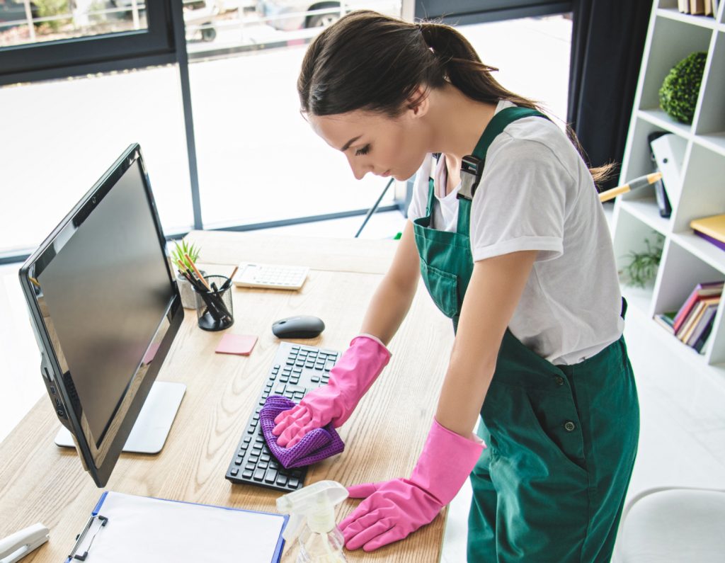 woman in green jumpsuit and gloves wiping keyboard