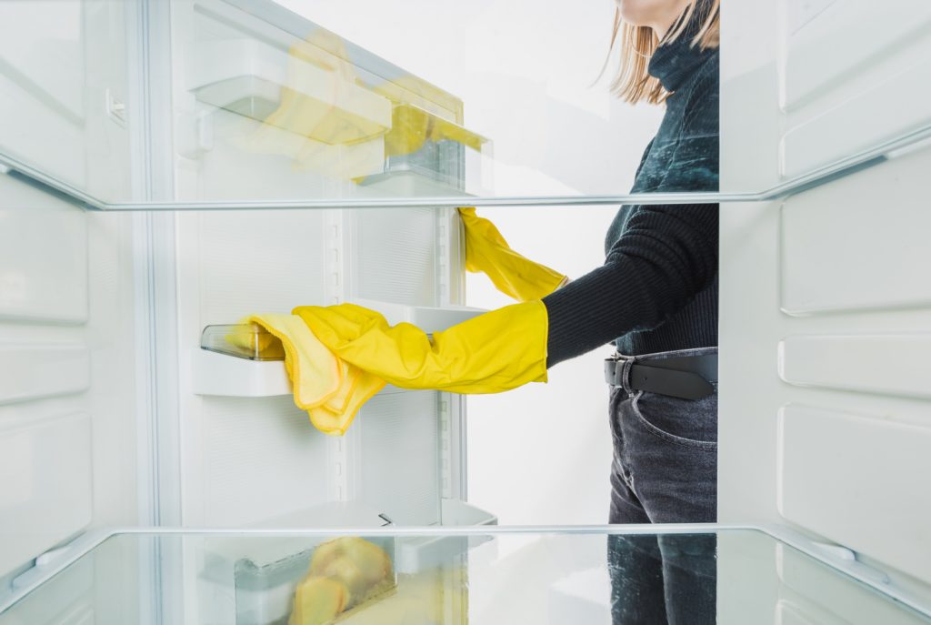 woman with yellow gloves cleaning the inside of her fridge
