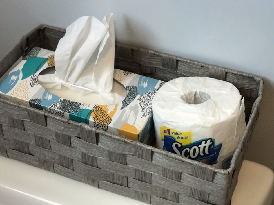 An image that shows a woven basket over the toilet that holds Kleenex and toilet paper. 