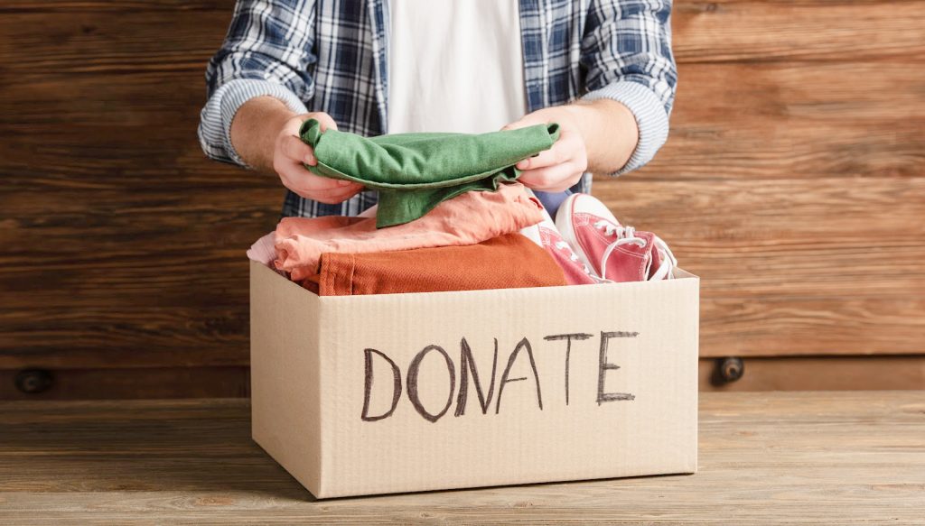 a person in a plaid shirt putting clothes into a donation box