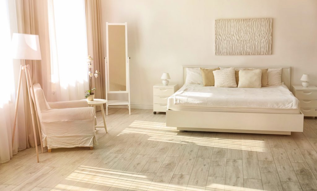 a simple bedroom with a cozy bed, chair and mirror